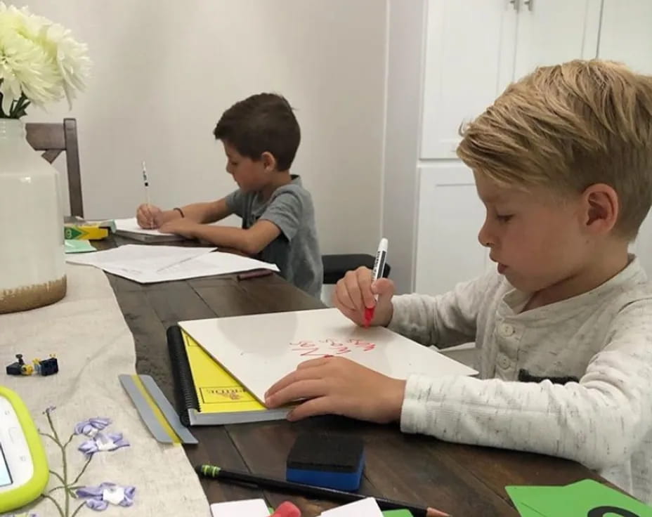 a few young boys sitting at a table writing on paper