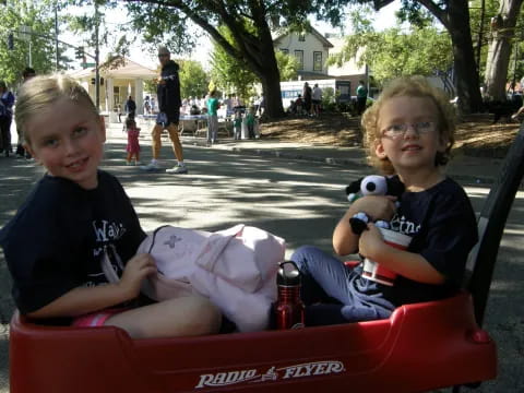 a couple of kids sitting in a red car with a stuffed animal