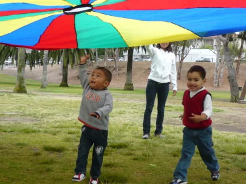 a couple of kids stand under a colorful umbrella