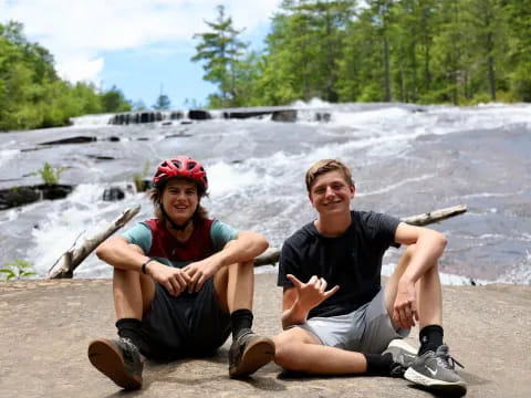 a man and woman sitting on a rock by a river