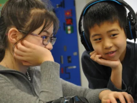 a boy wearing headphones and sitting next to a girl wearing a headset