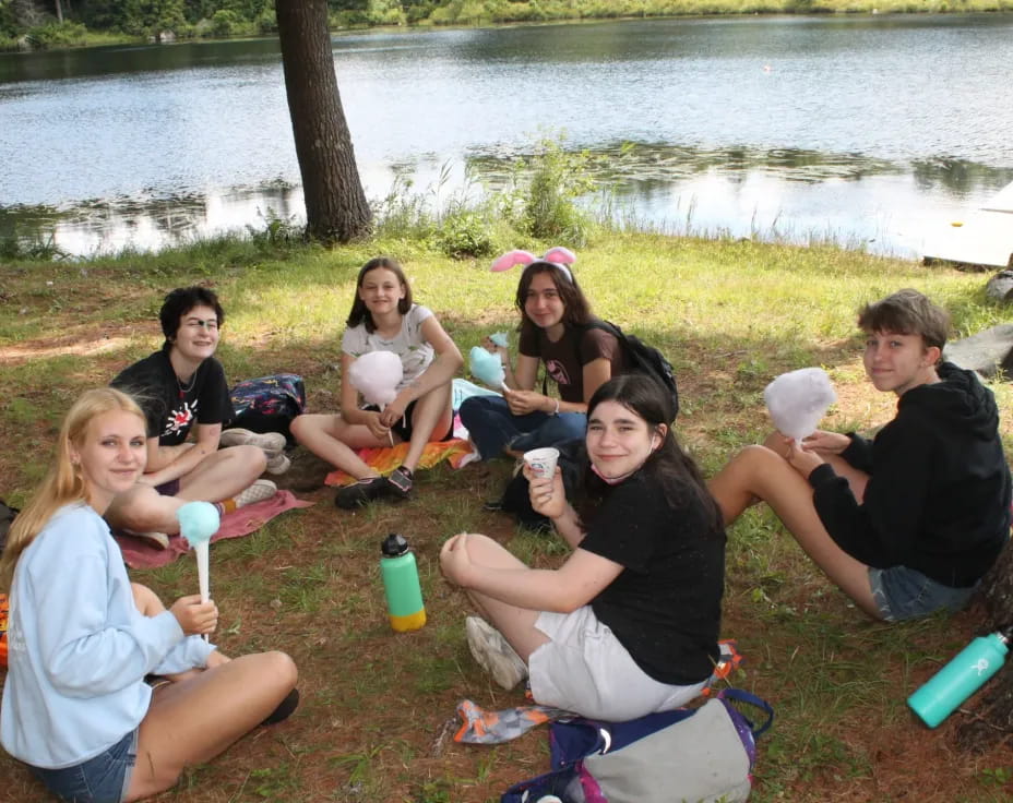 a group of people sitting on the grass by a lake