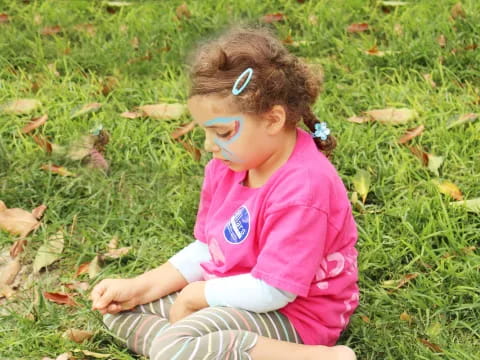 a little girl with paint on her face sitting in the grass