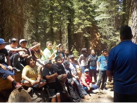 a group of people sitting on a log in the woods