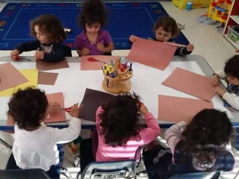 a group of children sitting at a table with colorful paper on it