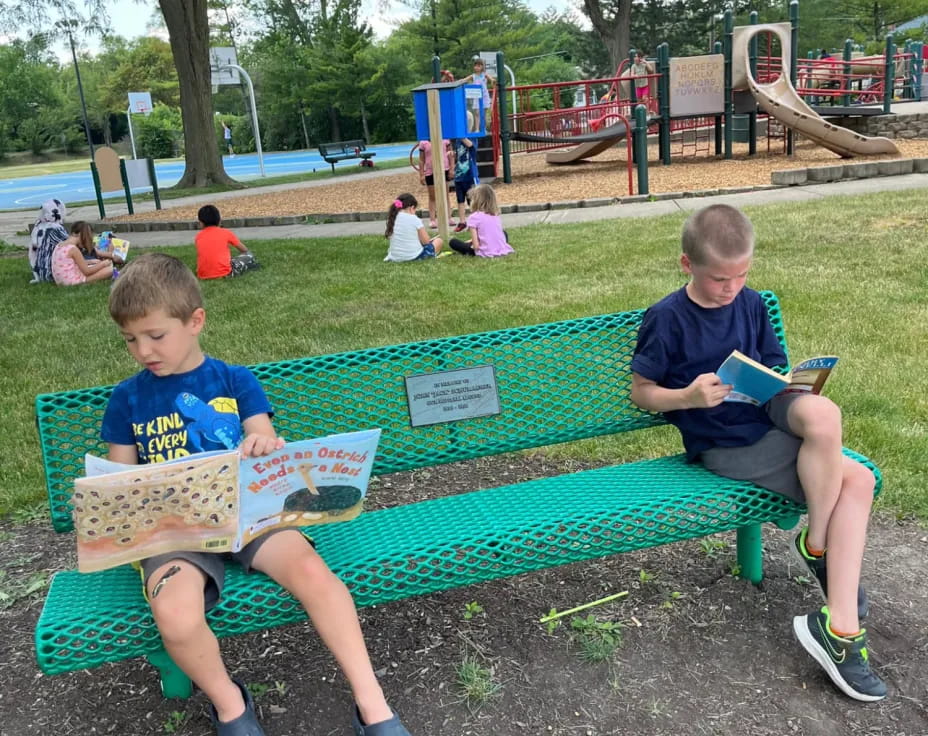 two boys sitting on a bench reading books