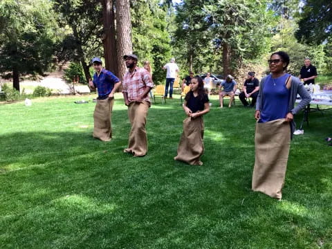 a group of people standing in a grassy area with trees and a table