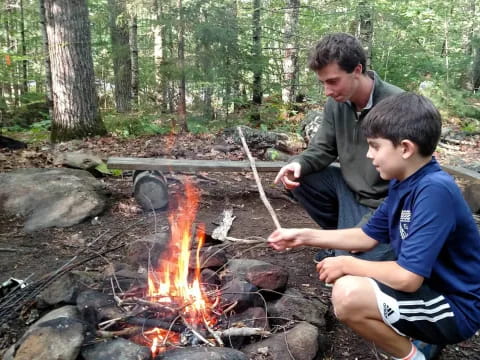 a couple of boys sitting by a fire in the woods