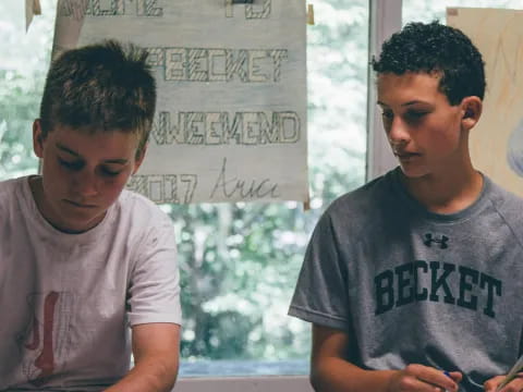 a couple of boys sitting at a table looking at a paper