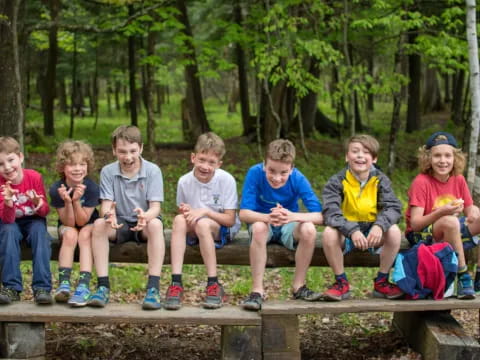 a group of kids sitting on a bench in the woods