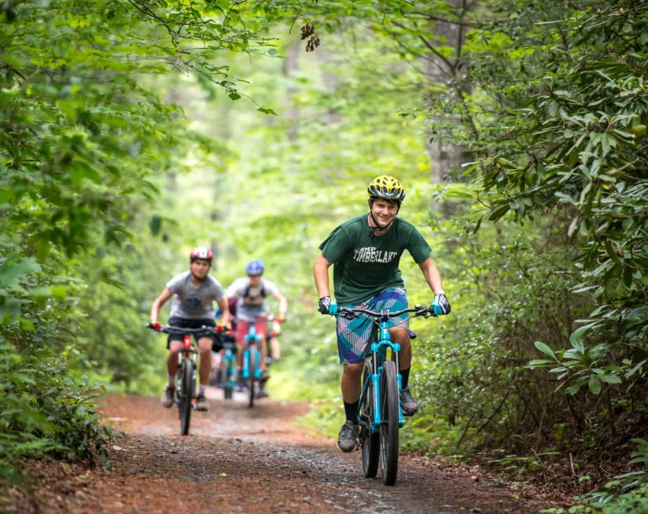 a group of people riding bikes on a dirt path in the woods