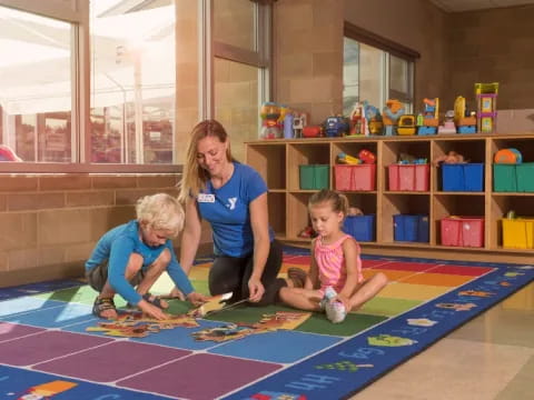 a person and two children playing on a mat in a room with shelves