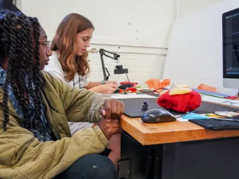 a woman and a man sitting at a desk looking at a computer screen