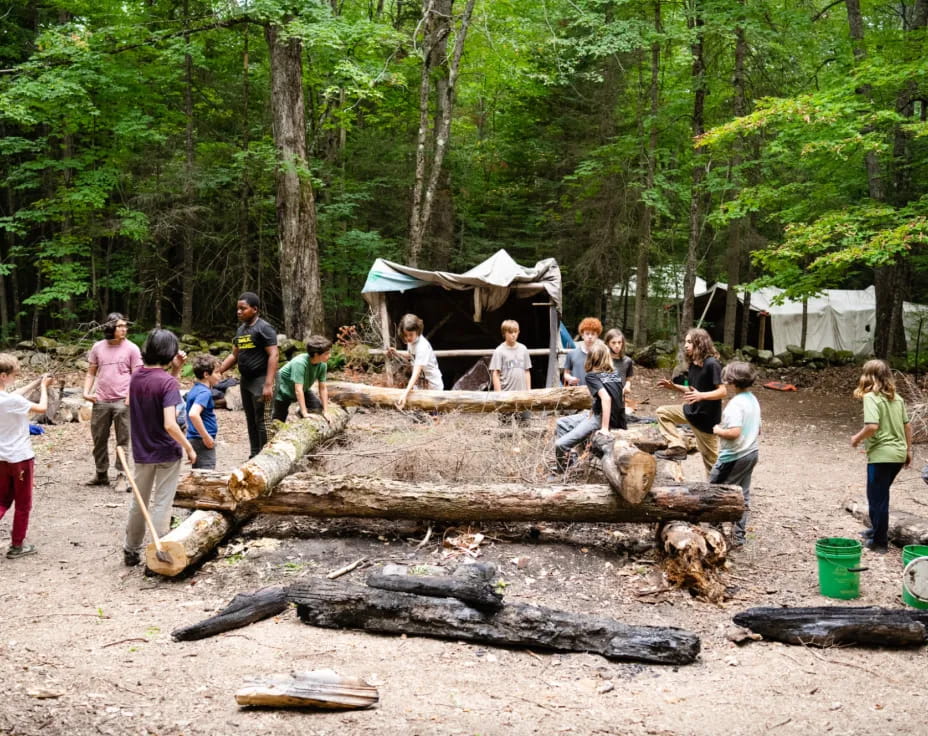 a group of people outside by a log in the woods