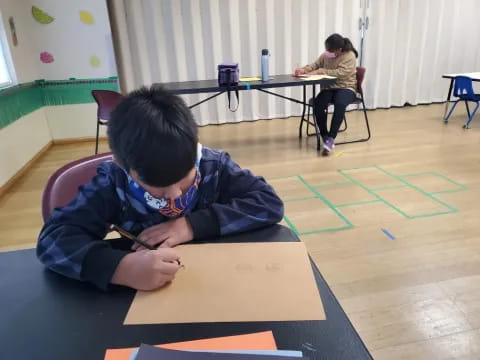 a boy sitting on the floor writing on a piece of paper
