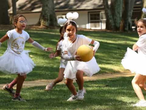 a group of girls in white dresses running with a ball