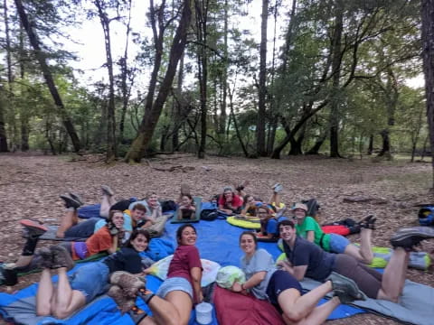 a group of people sitting on a blanket in a circle in the woods
