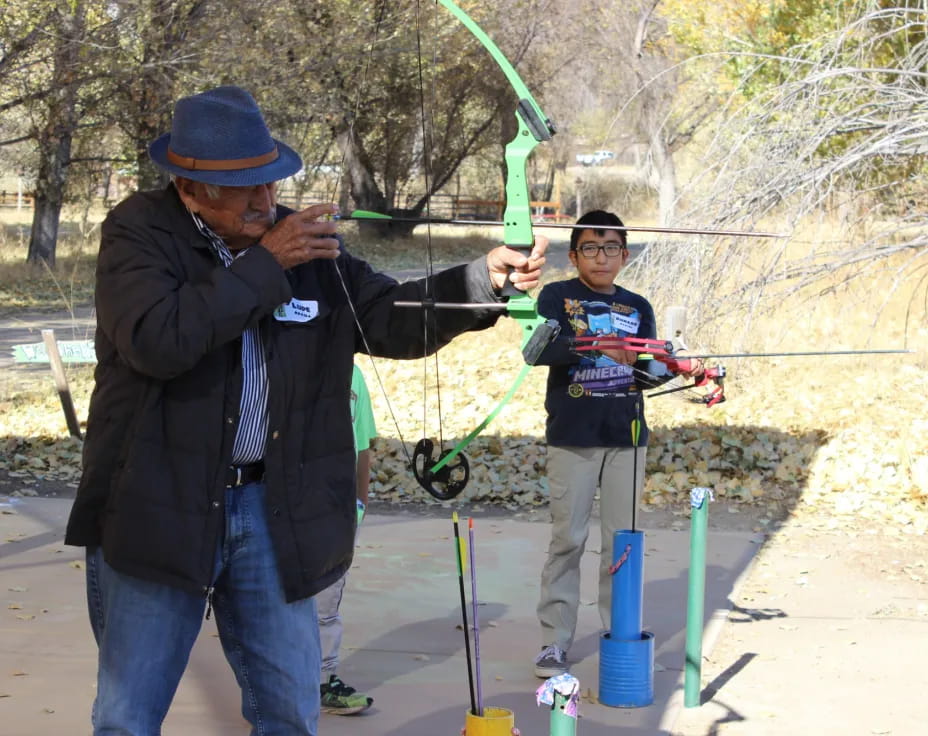 a person holding a bow and arrow next to a boy holding a bow