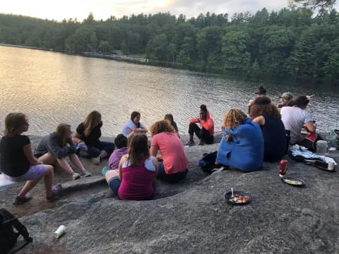 a group of people sitting on the ground by a lake