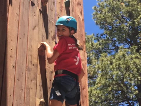a boy wearing a helmet and climbing a wooden fence