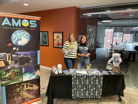 a couple of women standing next to a table with a display of items