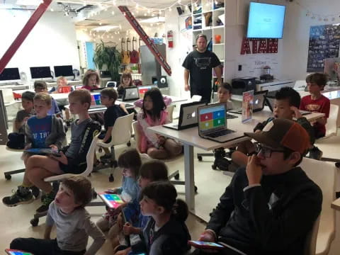 a group of children sitting at a table with laptops