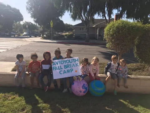 a group of children sitting on a bench holding a sign
