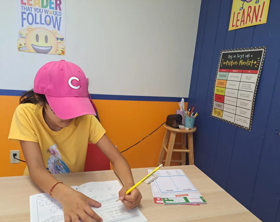 a girl sitting at a desk writing on a piece of paper