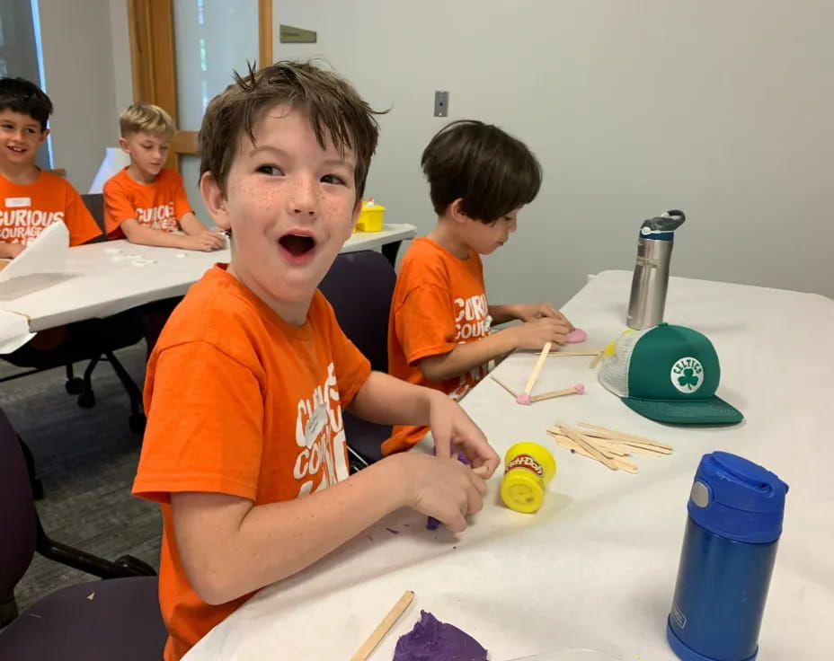 a group of kids sitting at a table with paint brushes