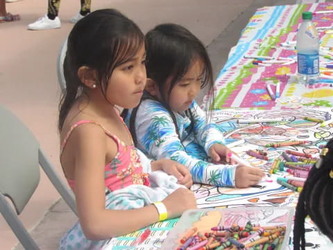 a couple of young girls sitting at a table with a colorful tablecloth