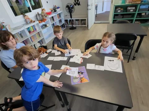 a group of children sitting around a table with a book and a toy