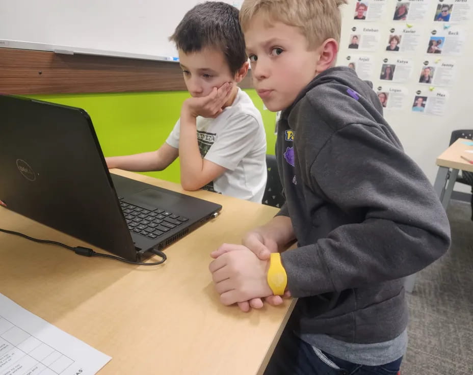 a couple of boys sitting at a table with a laptop