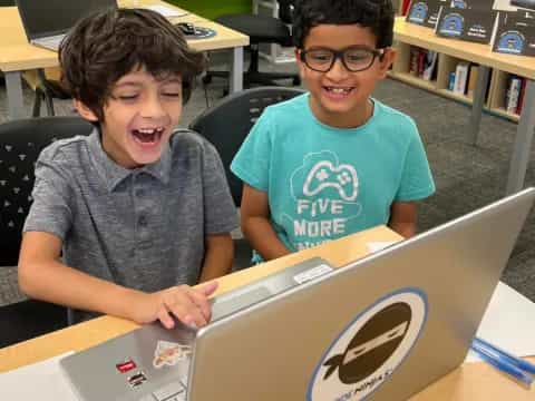 a couple of boys sitting at a table with a laptop