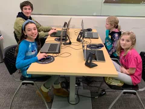 a group of children sitting at a table with laptops