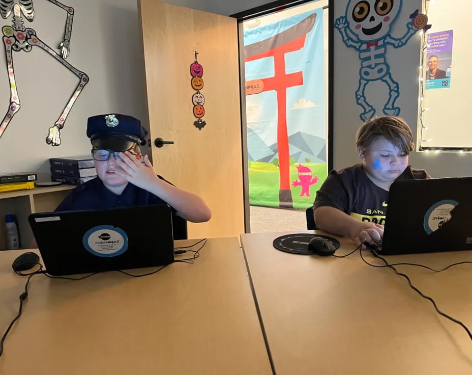 a couple of boys sitting at a table with laptops