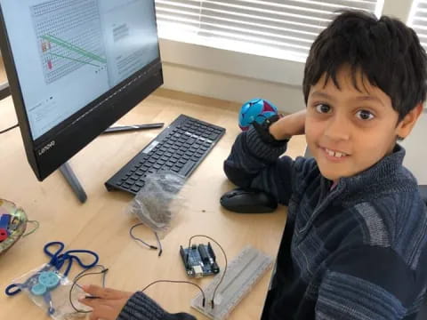 a boy sitting at a desk with a computer and a game controller