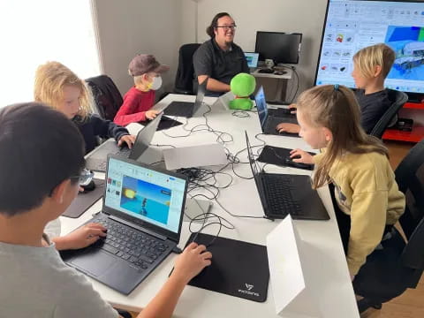 a group of people sitting at a table with laptops