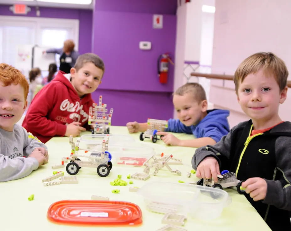 a group of boys sitting at a table with toy cars