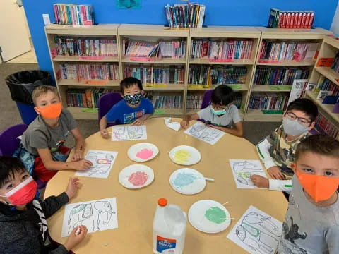 a group of children sitting at a table with paper plates and books
