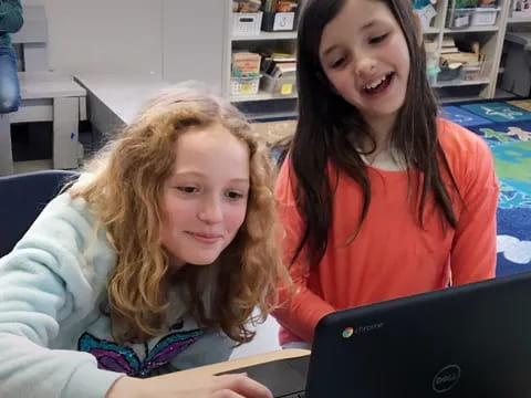 a couple of girls looking at a laptop