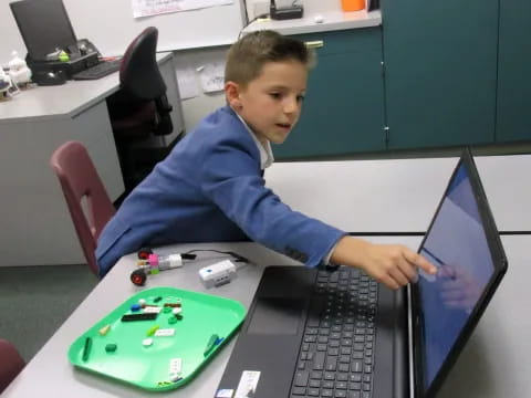 a boy sitting at a desk with a laptop and a toy