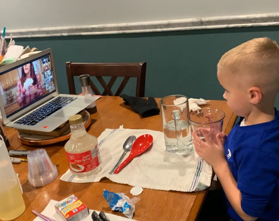 a kid sits at a table with a laptop and a glass of juice