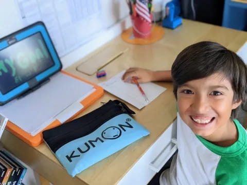 a boy sitting at a desk with a laptop and a pen