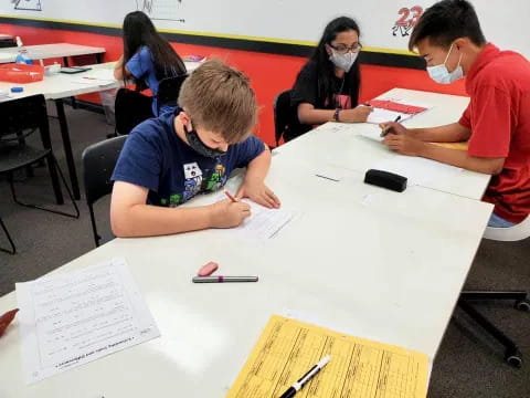 a group of people sitting at a table writing on paper