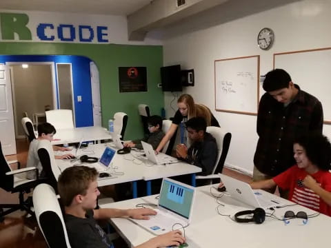 a group of people sitting around a table with laptops