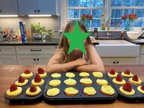 a woman sitting at a table with a bunch of cupcakes