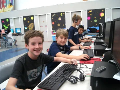 a group of kids sitting at a desk with computers