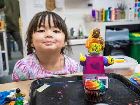 a girl sitting at a table with a cupcake and a toy