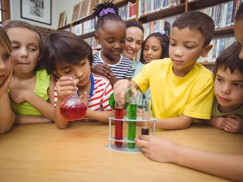 a group of children sitting at a table with a glass of liquid