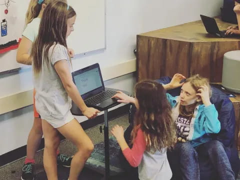 a group of children sitting in a classroom with a laptop